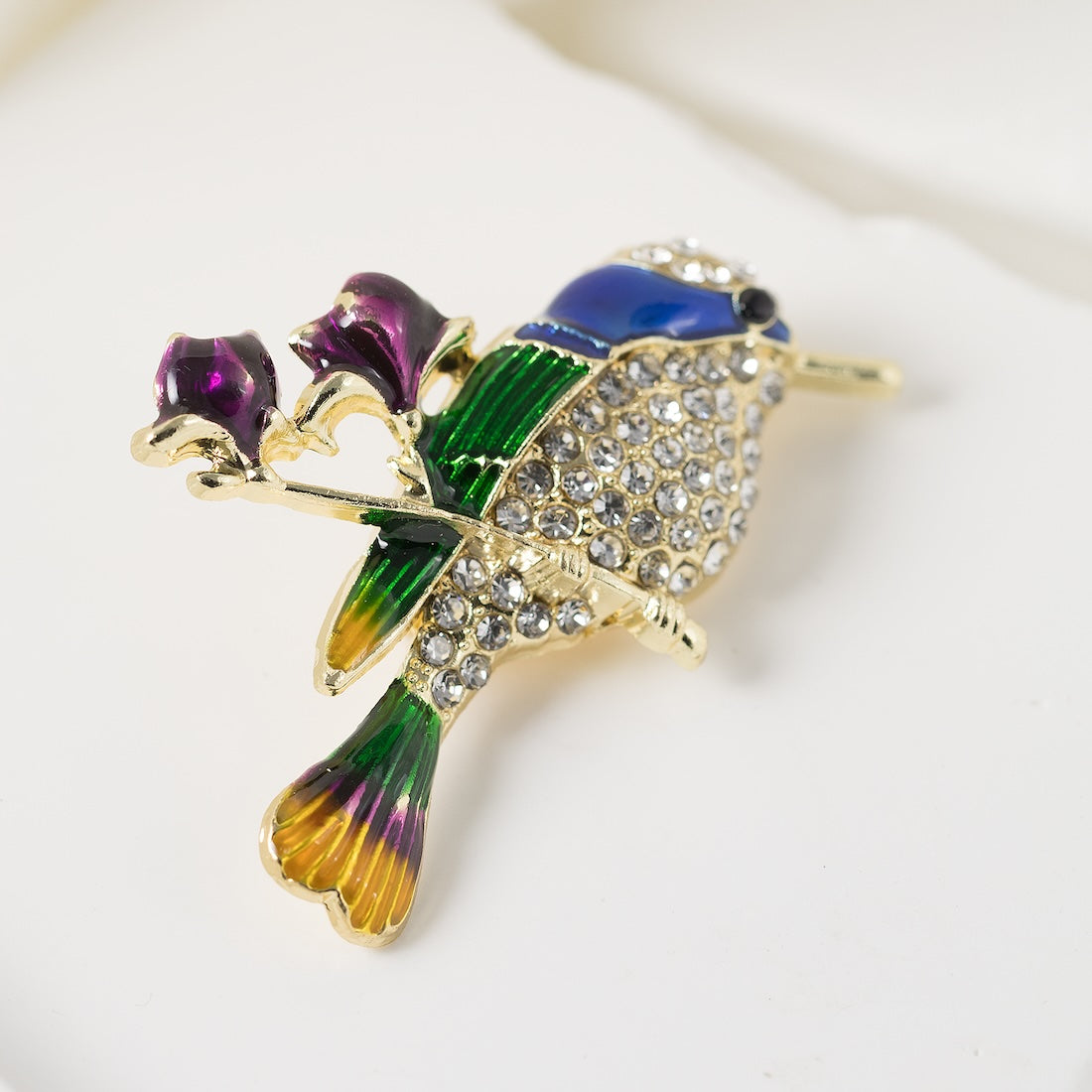 Eleganta piespraude kolibri formā ar krāsainiem kristāliem un metālisku apdari.